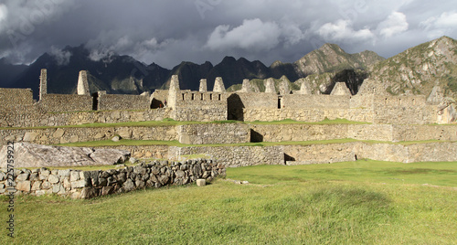 stone ruins in bright sunlight with dark mountiains in shade, Machu Picchu, Peru photo