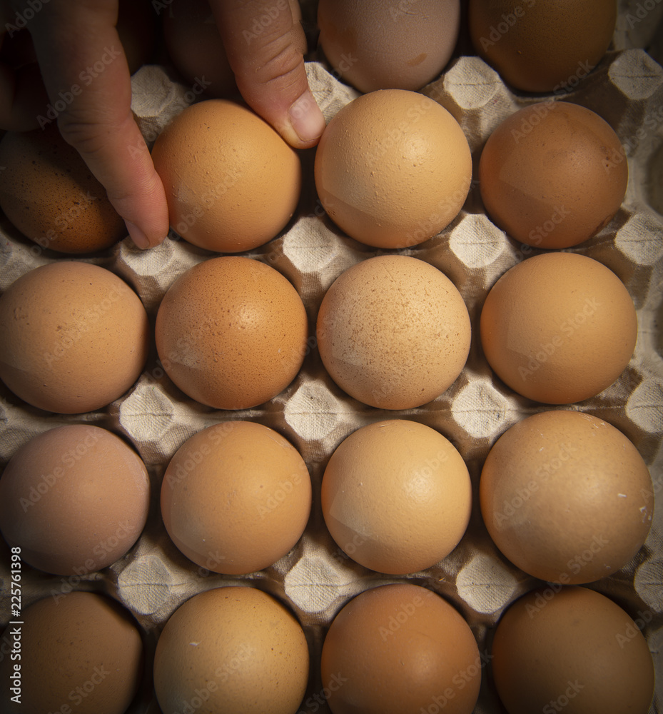 Brown eggs in carton box, Broken egg with yolk in background Brown eggs in carton box, Broken egg with yolk in background