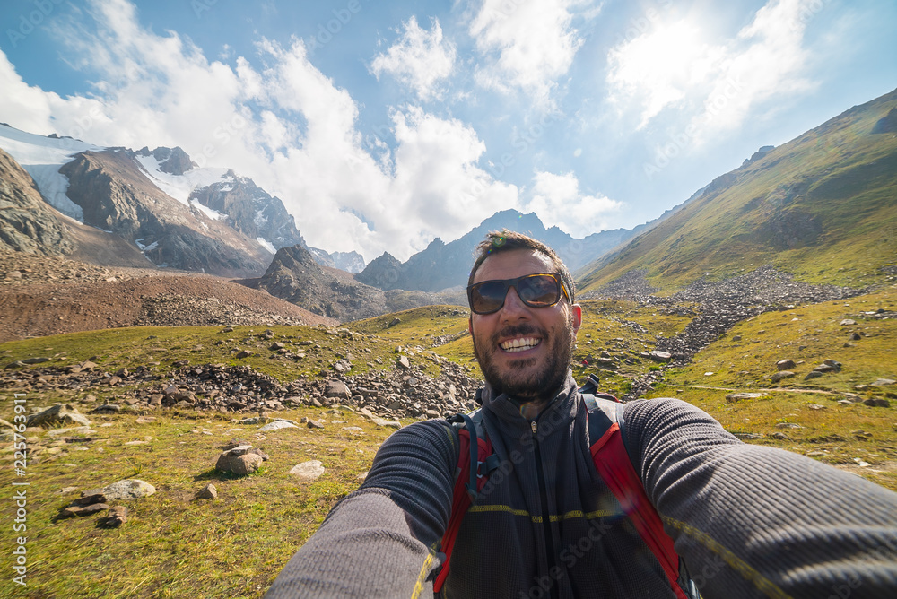 Self-portrait of a handsome young hiker in the top of the mountain with amazing landscape in background, kyrgyzstan, central asia