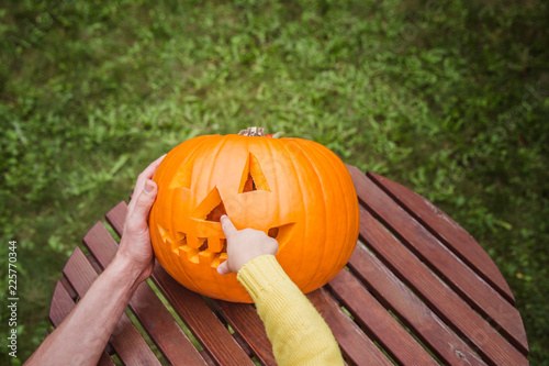 Happy halloween. Father and small daughters look at the face cut in the pumpkin high angle view. Small giirl show a nose of pumpkin Jack O Lanterns. Outside. photo