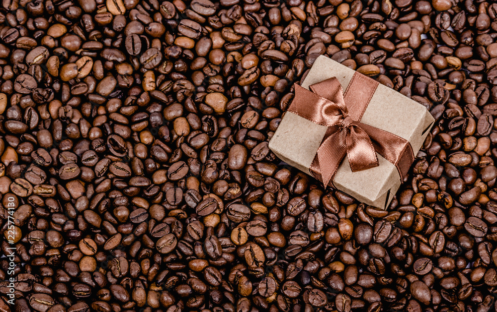 Gift box with ribbon on coffee background. Roasted coffee beans background. Copy space