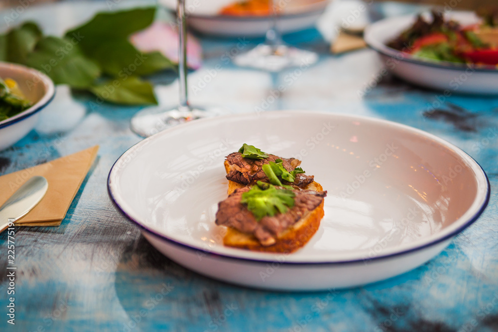 Bruschetta on a white plate in a restaurant. With meat