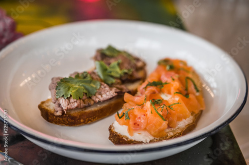 Two bruschetta on a white plate in a restaurant. With fish and meat