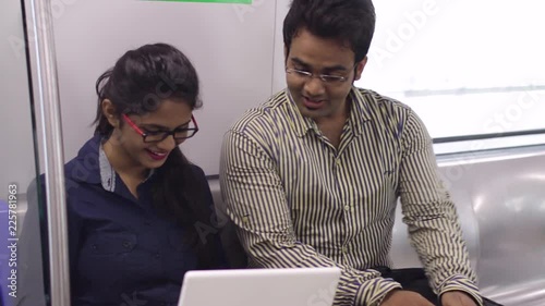Young Indian office going boy and girl together in a metro train using a laptop.