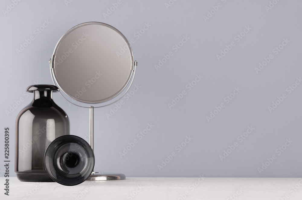 Soft light elegant home decor in minimalist slyle - black transparent vase, glass, circle mirror on grey wall and white wood background. Soft light elegant home decor in minimalist slyle - black transparent vase, glass, circle mirror on grey wall and white wood background.
