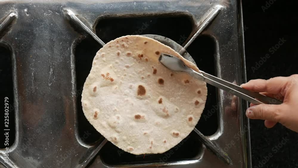 footage of making of Phulka a kind of Chapati: Indian thin bread made from wheat dough being baked on gas stove in home.