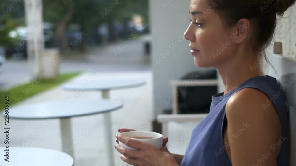Portrait of lovely girl looking at camera Attractive young pensive woman holding a cup and looking away while sitting outside coffee shop. Portrait of lovely girl looking at camera Attractive young pensive woman holding a cup and looking away while sitting outside coffee shop.