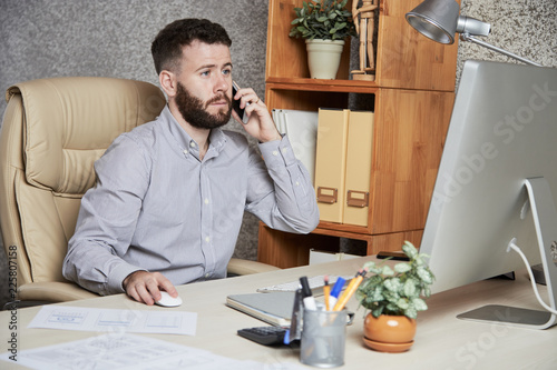 Concerned business executive talking on phone and reading data on computer screen