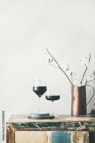 Two glasses of red wine and flowers over rustic kitchen countertop, white background behind, copy space. Wine shop, winery, bojole nouveau holiday concept photo