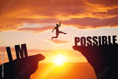 Man jumping over impossible or possible over cliff on sunset background photo