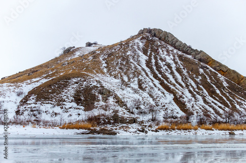 The snowy hill with the rocky crest on the top and icy surface in front of it. Two Sisters mountain, Belaya Kalitva town, Seversky Donets river, Russia photo