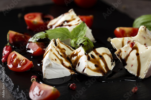 Pieces of camembert cheese with cherry tomatoes balsamic vinegar on a dark slate