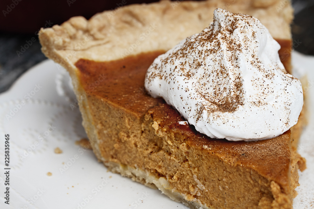 Slice of homemade pumpkin pie with topping and sprinkled with pumpkin pie spice. Extreme shallow depth of field with selective focus on whipped cream. Slice of homemade pumpkin pie with topping and sprinkled with pumpkin pie spice. Extreme shallow depth of field with selective focus on whipped cream.