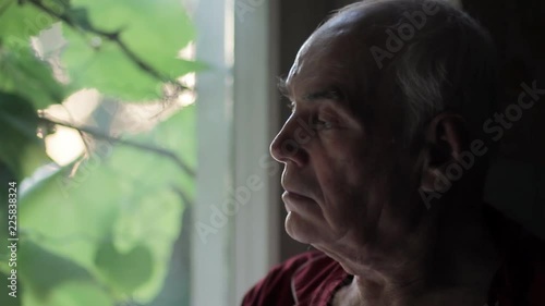Portrait of sad lonely elderly man looking out of the window at sunset. Loneliness and depression in old age. photo