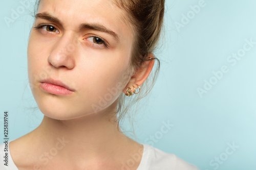 emotion face. suspicious thoughtful dubious skeptic distrustful woman. young beautiful brown haired girl portrait on blue background.