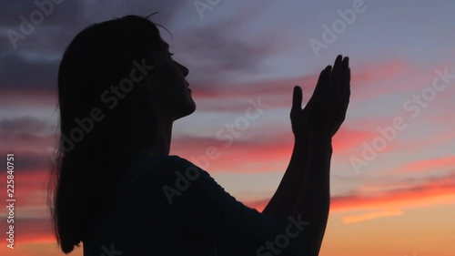 Praying woman looking up raising open hands to sky. Female prayer silhouette colorful sunset