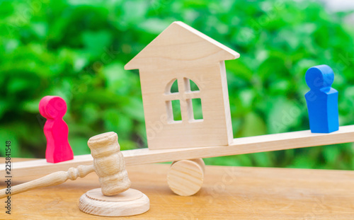 division of property by legal means. clarification of ownership of the house. wooden figures of people. man and woman are standing on the scales. trial, conflict. court. divorce