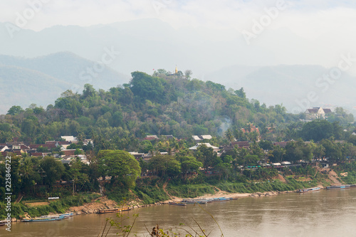 Moored boats on the Mekong River, city of Luang Prabang, Mount Phousi (Phou Si, Phusi, Phu Si) and mountains in the background viewed from the Chomphet District on a sunny day in Laos. photo