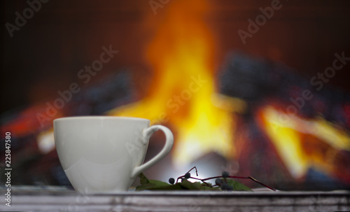 Cup of tea on a wooden table with bright autumn leaves and heart cookies on the background of the fireplace