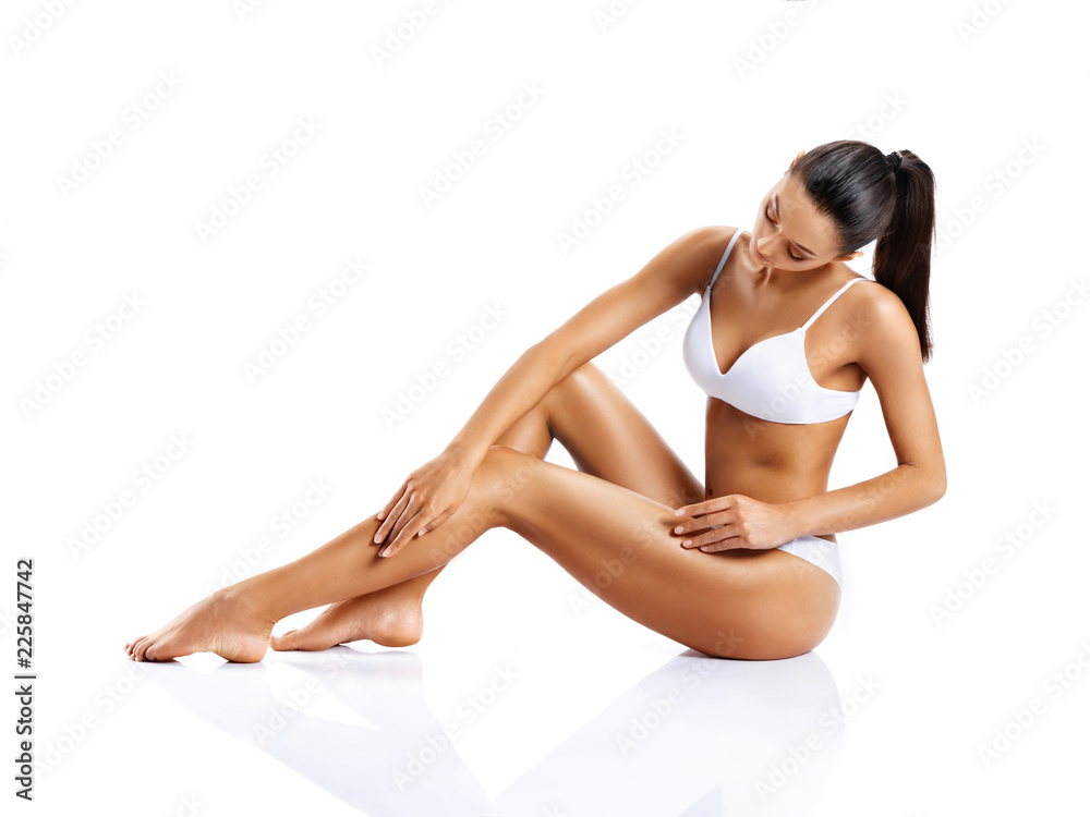 Young girl with perfect body touching her leg sitting on white background. Beauty & Skin care concept