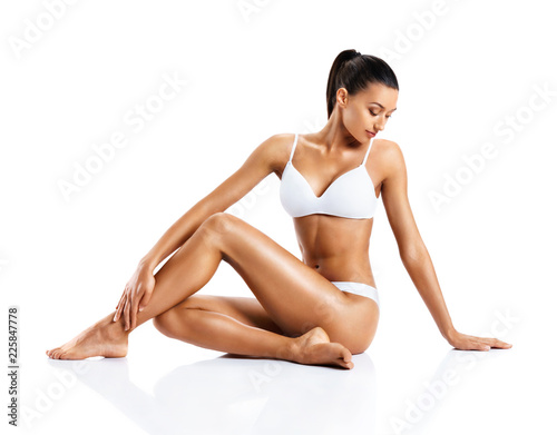 Beautiful girl touching her healthy skin. Photo of young girl sitting on white background. Beauty and body care concept