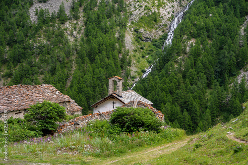 alpine village church and mountain waterfall at background
