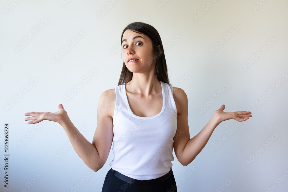 Shocked confused young woman shrugging shoulders and looking at camera. Emotional woman demonstrating ignorance and biting lip. Indifference concept Shocked confused young woman shrugging shoulders and looking at camera. Emotional woman demonstrating ignorance and biting lip. Indifference concept
