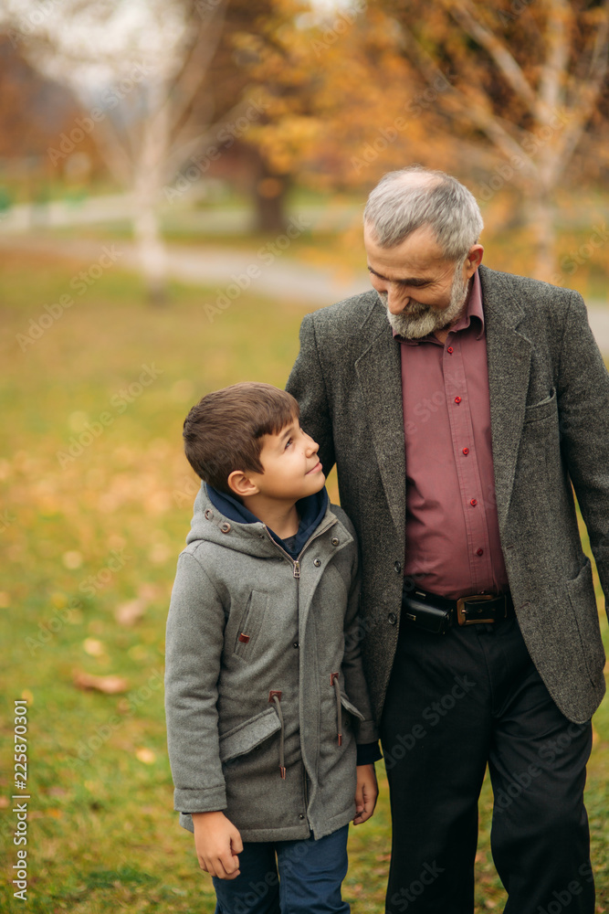 Grandpa and grandson spend time in autumn park. They hug each other and walk. Fmily time