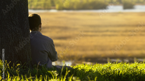 Photography young man sitting with his back to the tree and meditating about life, the conce