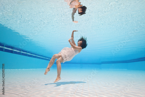 Photography Young attractive girl swim underwater in swimming pool in pink dress