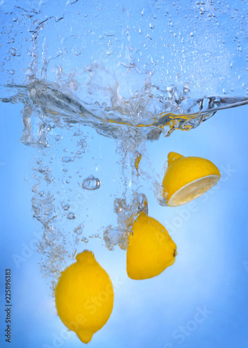 Tropical fruits fall deeply under water with a big splash lemon drop into water splashing on blue backgfround photo