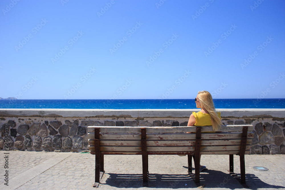 Young woman yellow t-shirt resting on the seafront on a wooden bench.