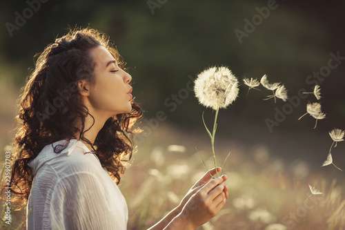 Canvas-taulu Beautiful Young Woman sitting on the field in green grass and blowing dandelion