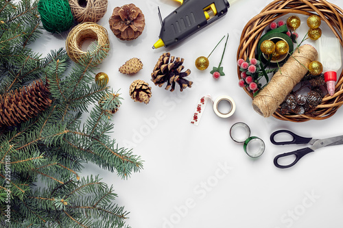 Preparing for Christmas or New Year holiday. Flat-lay of fur tree branches, wreaths, rope, scissors, craft paper over white table background, top view.