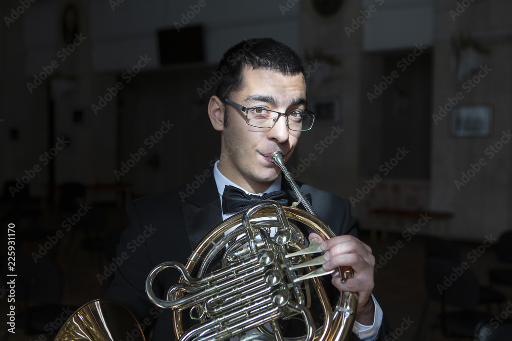 Fototapeta premium French horn player. Hornist playing brass orchestra music instrument.