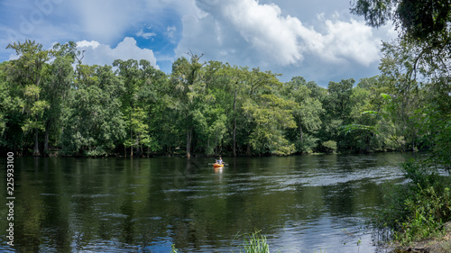 Young couple man and woman photographer kayaking down Santa Fe river in Florida in a yellow kayak with a forest landscape as background