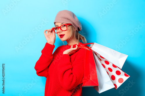 Portrait of a young girl in red sweater with shopping bags on blue background