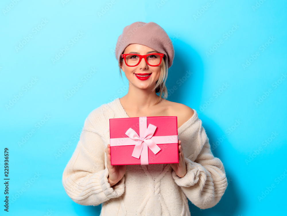 Portrait of a young girl in white sweater with red gift box on blue background Portrait of a young girl in white sweater with red gift box on blue background