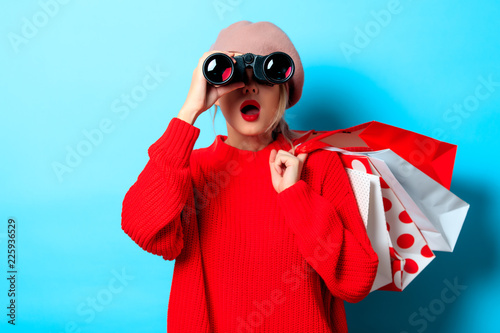 Portrait of a young girl in red sweater with bonocular box and shopping bag on blue background photo