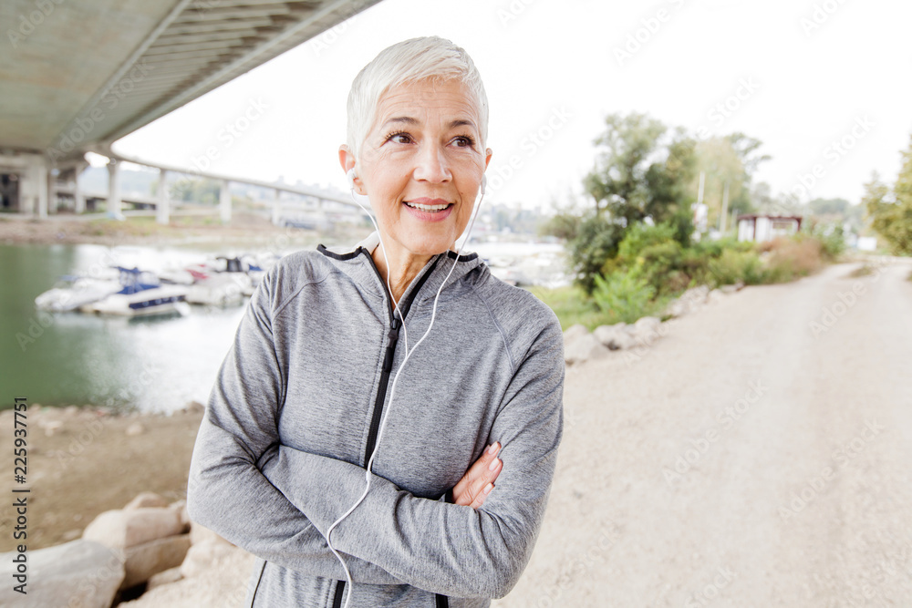 Fototapeta premium Smiling Senior Woman With Earphones Listening Music Workout