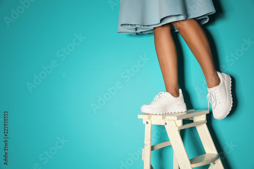 Woman in stylish sneakers on ladder near color wall, closeup. Space for text