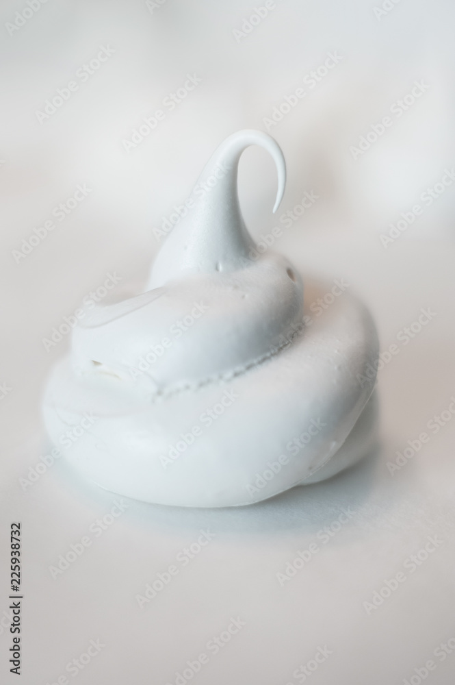 A white homemade meringue on white with blurry meringues behind. Shallow depth of field. Vertical image. A white homemade meringue on white with blurry meringues behind. Shallow depth of field. Vertical image.