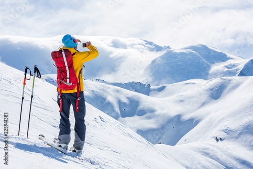 A skier is standing on the top. Sunny weather, clouds amd mountains.