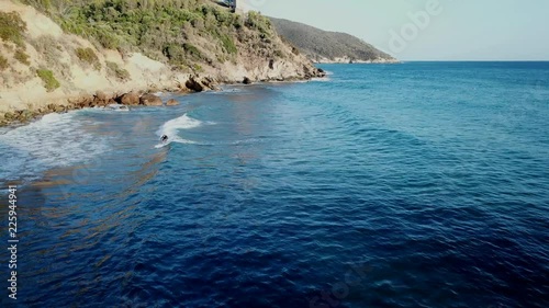 Aerial view of a surfer in a rocky mediterranean bay at the sunset time
