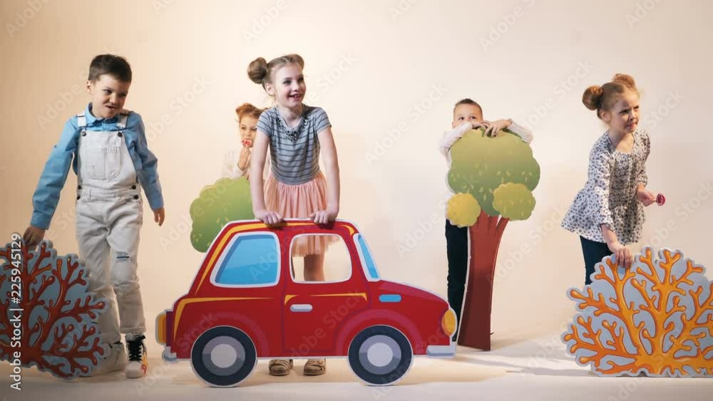 funny children are running with different decorations in the form of cars, trees and bushes on a studio background funny children are running with different decorations in the form of cars, trees and bushes on a studio background
