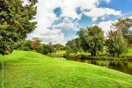 Green lawn and trees at river under blue cloudy sky.