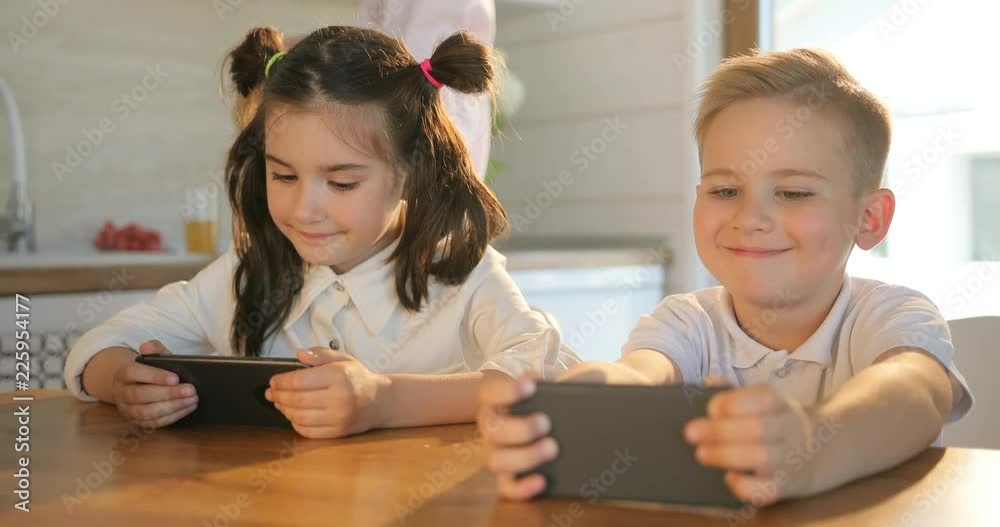 Cute brother and sister enjoying smart phone at home. Child girl and boy playing with a digital tablet. A smart phone holding, watching in hand children. Cute brother and sister enjoying smart phone at home. Child girl and boy playing with a digital tablet. A smart phone holding, watching in hand children.