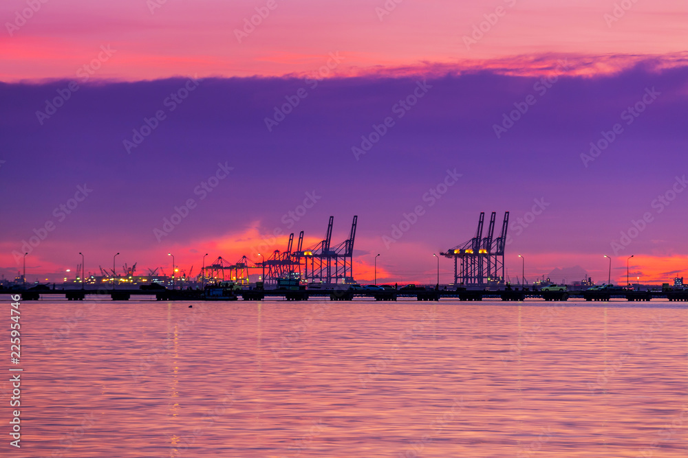 Fototapeta premium Logistics and transportation of Container Cargo with working crane bridge in shipyard. Cargo shipping and commercial terminal in seaport at sunset. Industrial landscape with gantry cranes in sea port.