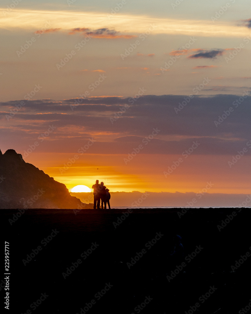 A Chilean family taking photos and enjoying the amazing sunset in between the cliffs, the forest and the beach while they are looking at the sunset on a cloudy day at Buchupureo beach, Chile
