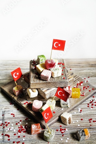 various national Oriental sweets, with paper flags of Turkey, Turkish delight on a wooden white brushed stand and on a white brushed background, vertical, the concept of the independence day of Turkey